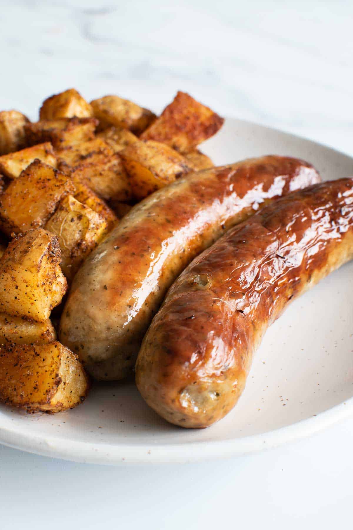 Baked brats and potatoes on a plate.
