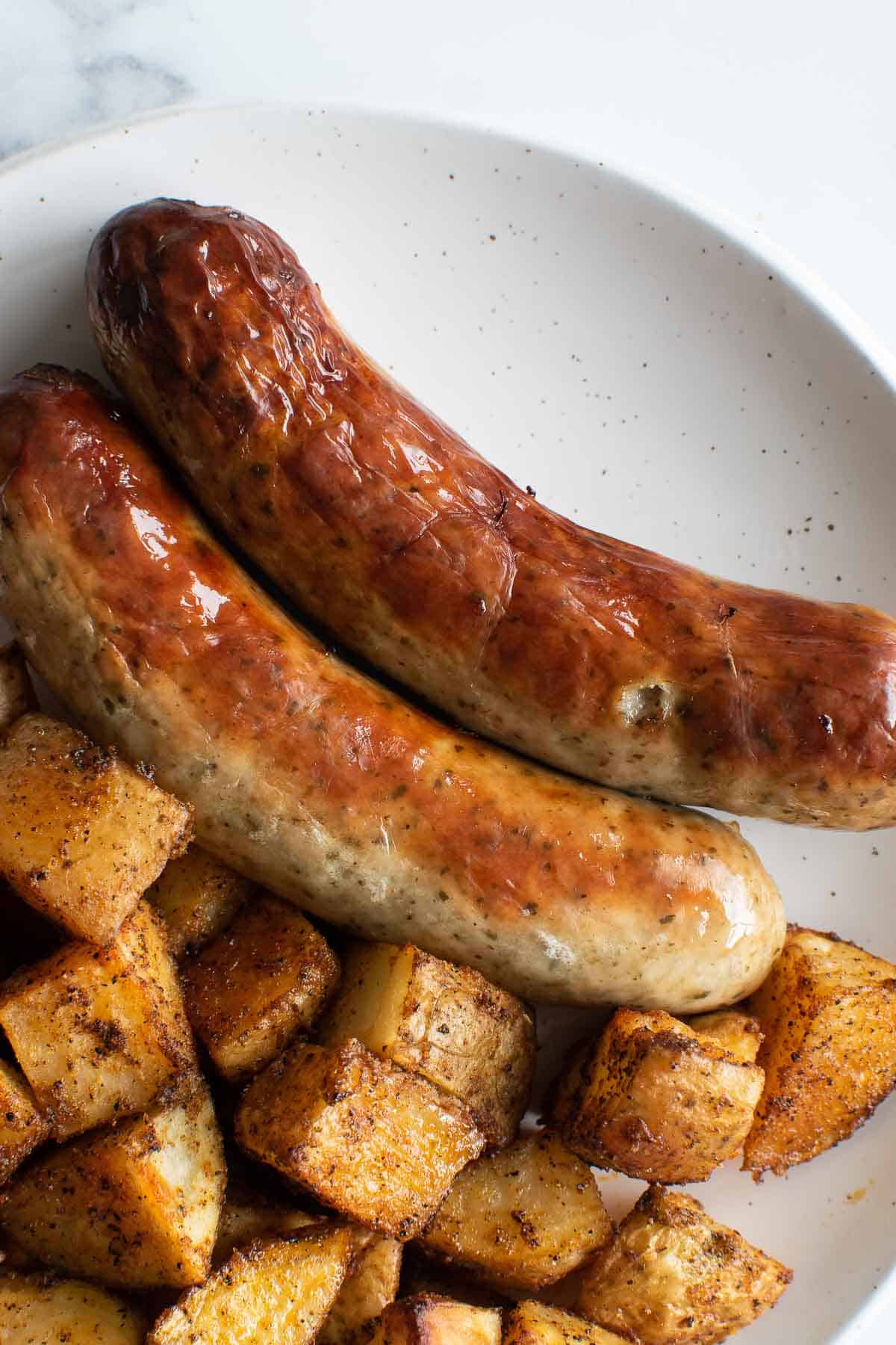 Bratwurst sausages on a plate with roasted potatoes.