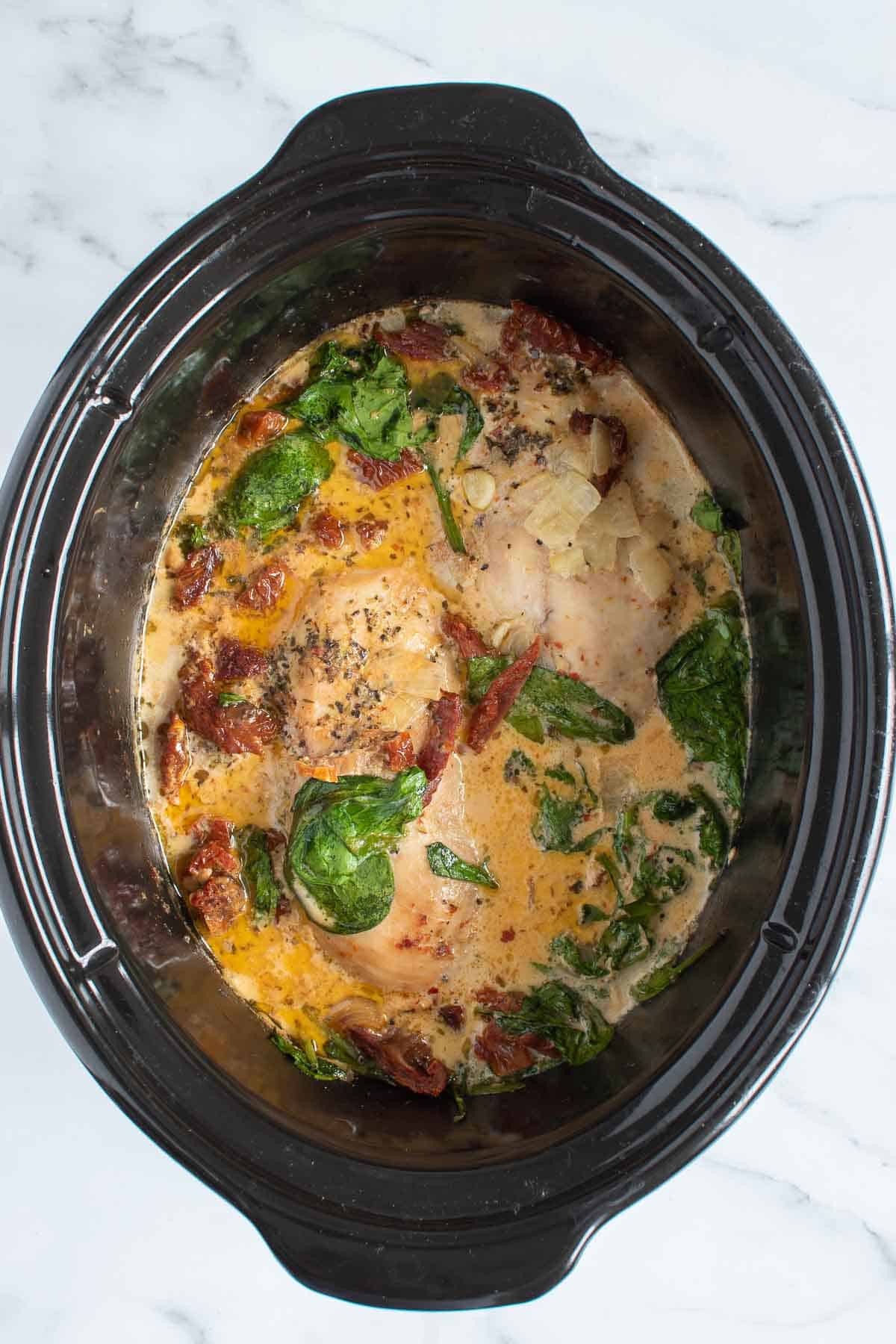 A Crockpot with chicken, cream, spinach and sun dried tomatoes.