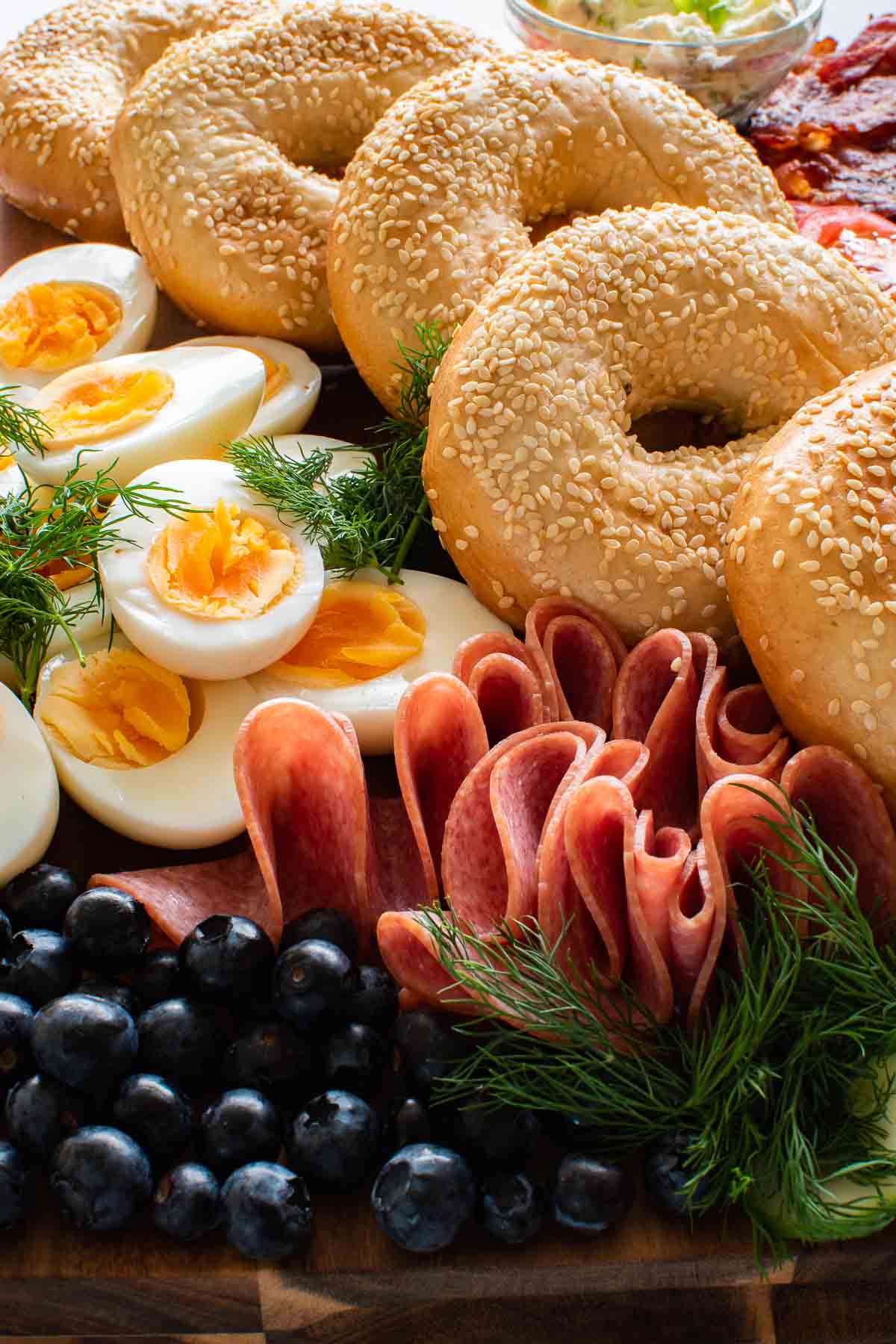 Bagels on a grazing platter with boiled eggs, salami, dill and blueberries.