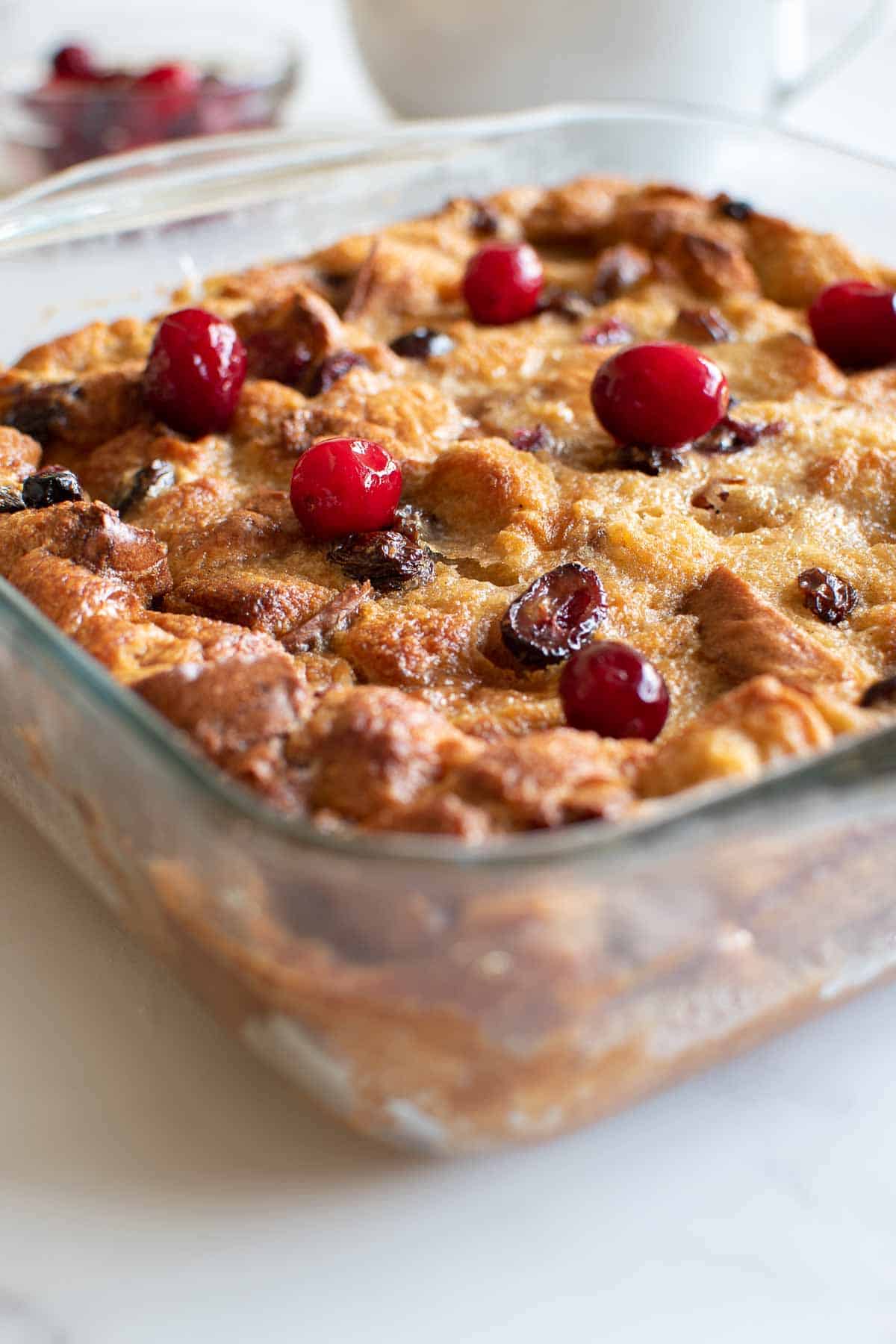 A casserole dish of eggnog bread pudding, garnished with cranberries.
