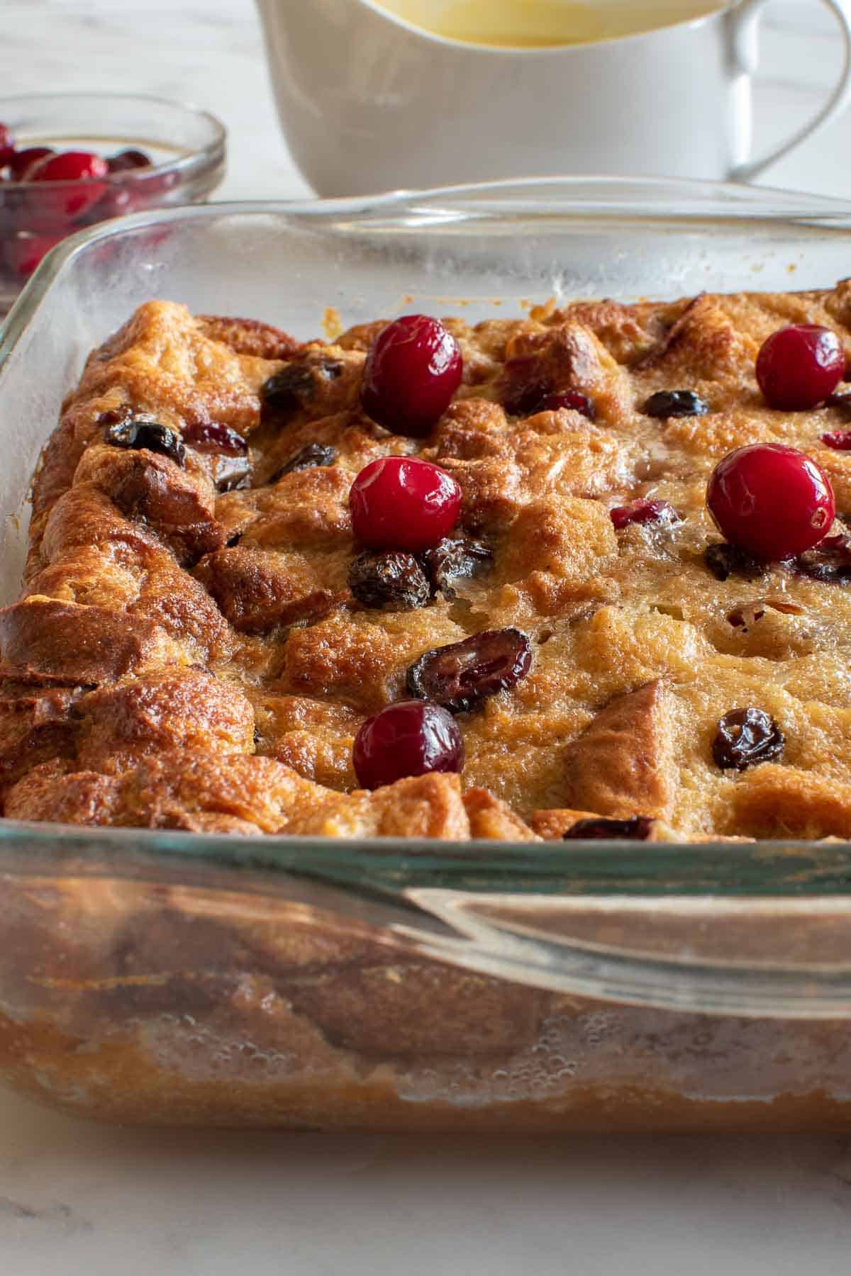 Bread pudding with eggnog and cranberries, with custard in the background.