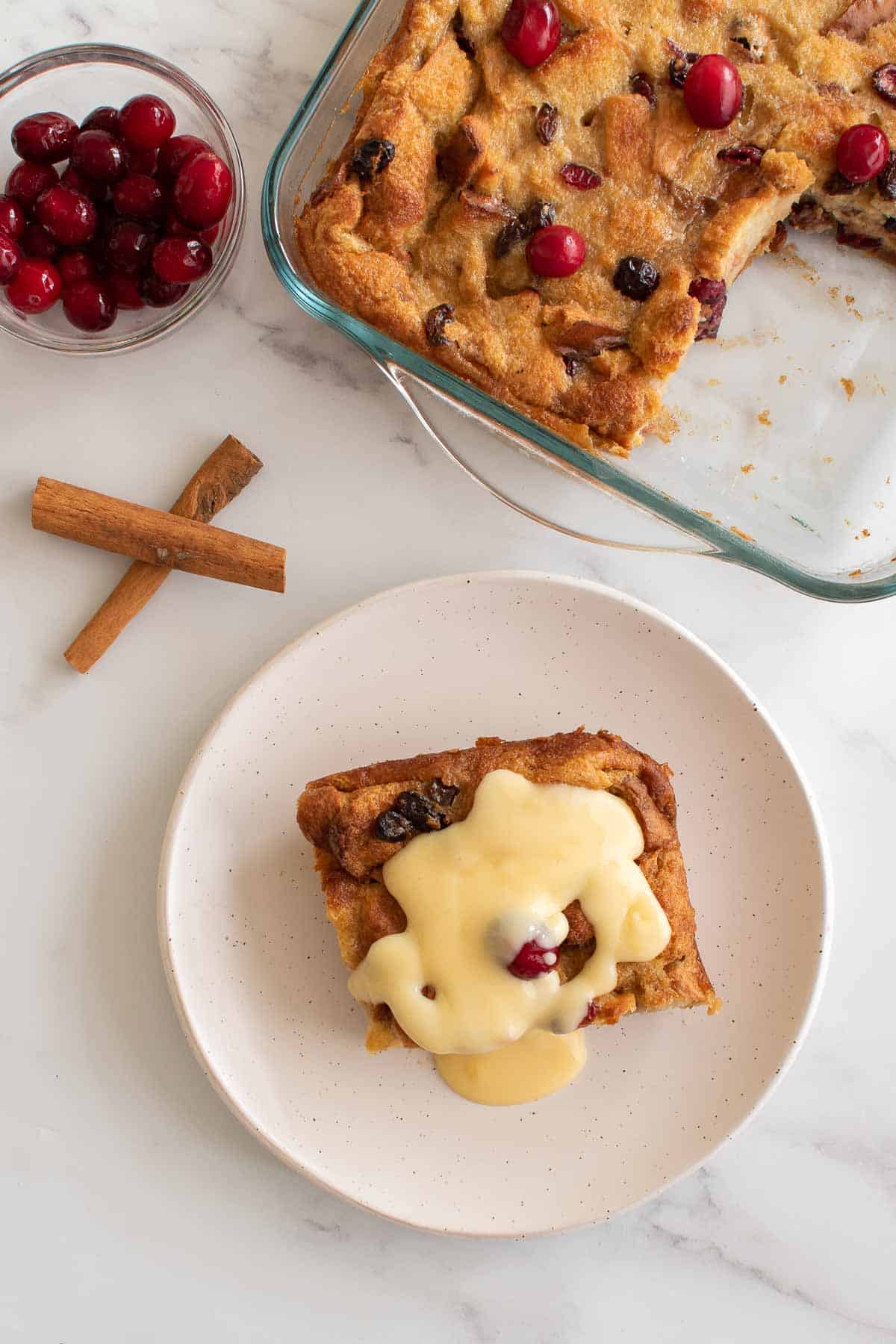 Bread pudding in a dish, with one plated serving with eggnog bread pudding and custard on the side.