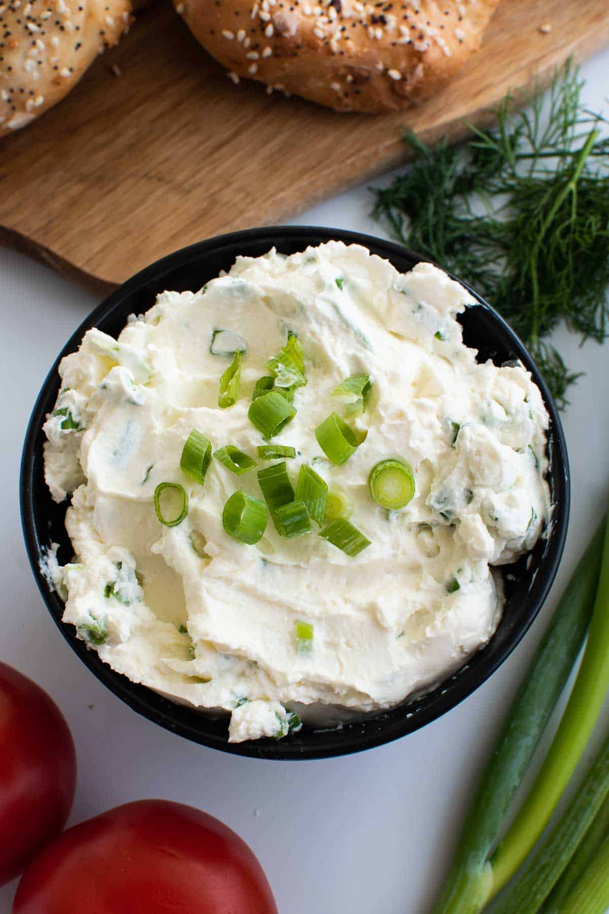 Cream cheese spread with scallions, with herbs and bagels on the side.