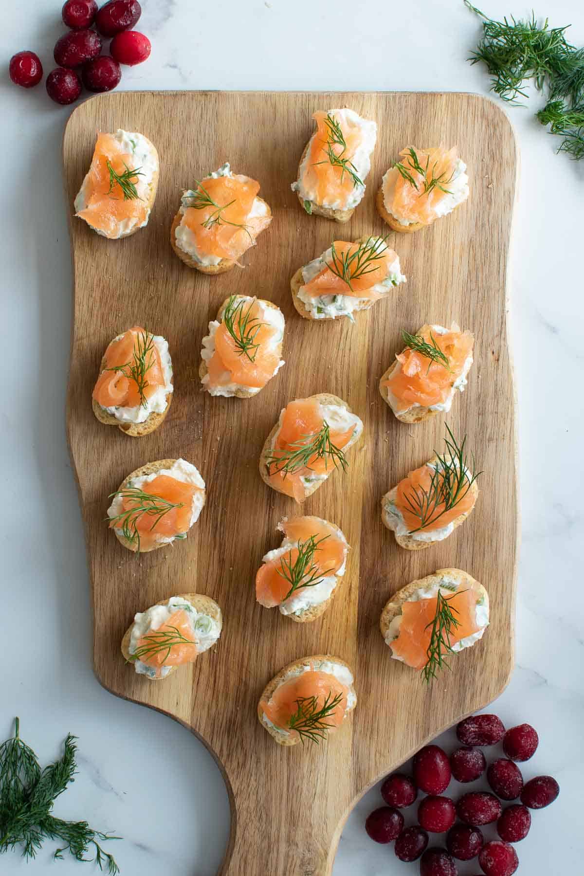 Canapes with cream cheese, dill and smoked salmon on a cutting board with cranberries on the side.
