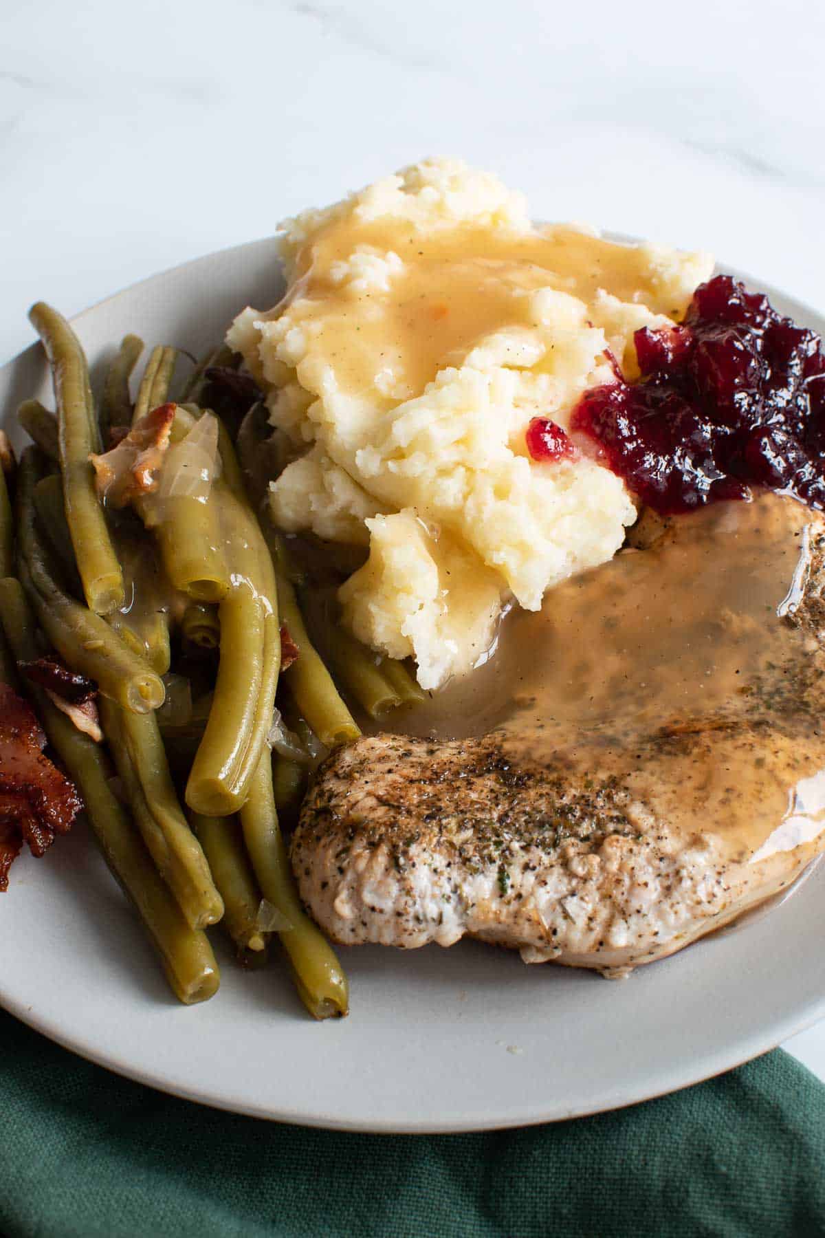 A plate with turkey steaks, mash, green beans and cranberry sauce.