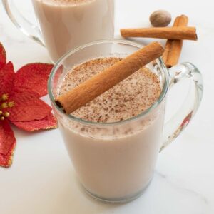 A cup of eggnog with cinnamon sticks on the side.