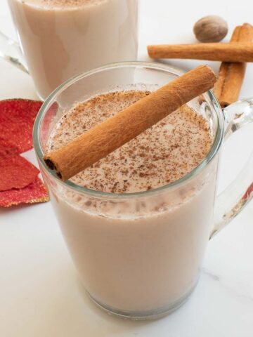 A cup of eggnog with cinnamon sticks on the side.