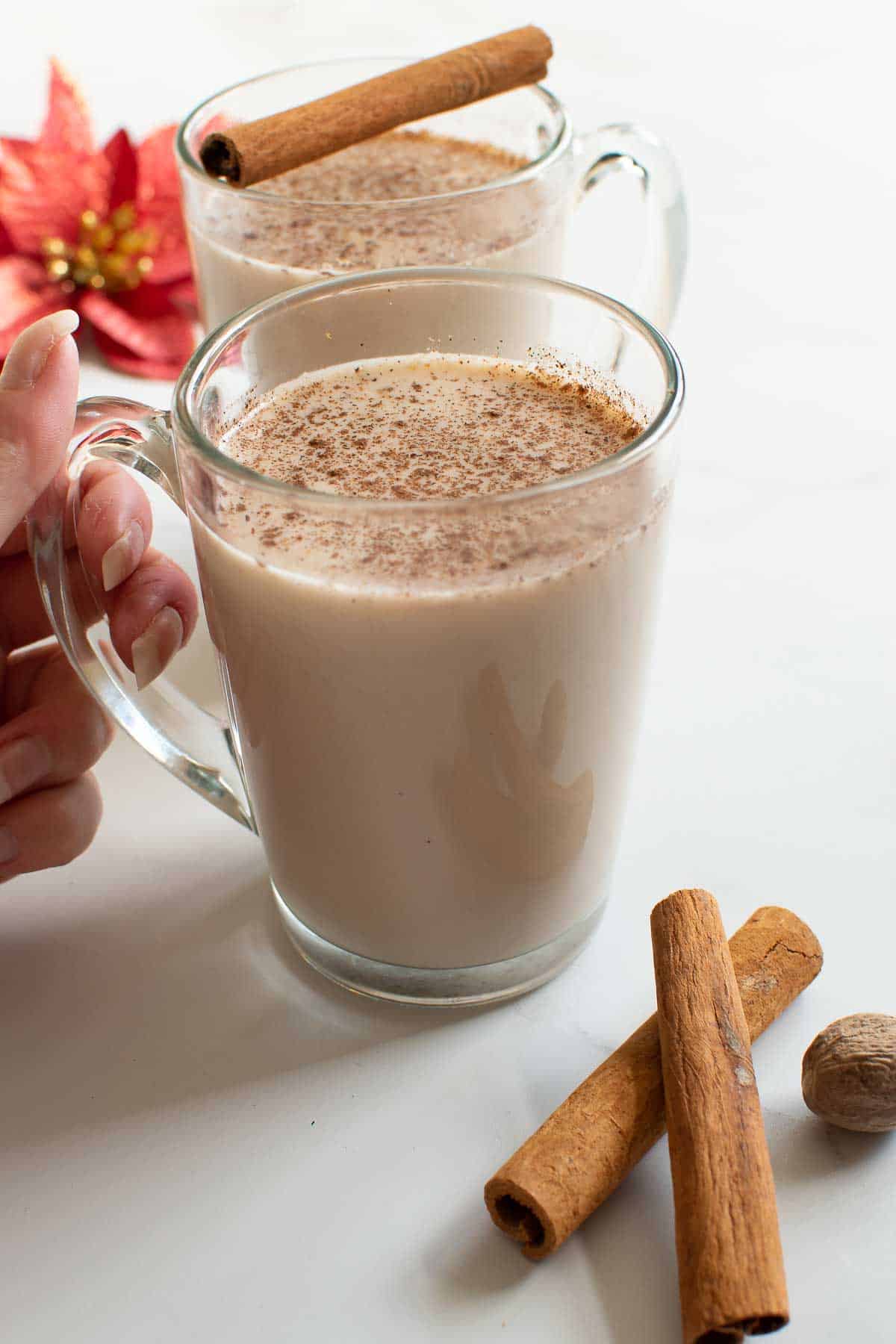 A hand lifting up a glass with warm eggnog.