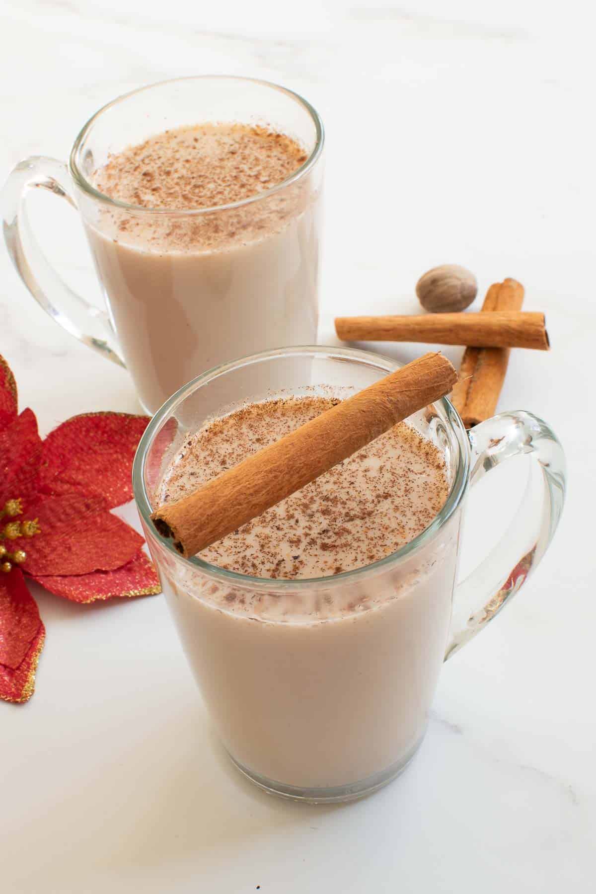 Two cups of egg free eggnog, decorated with cinnamon sticks.