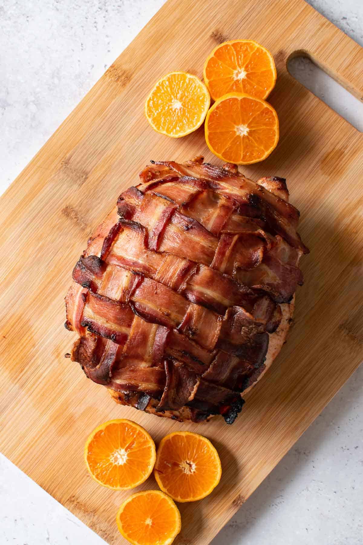 Bacon wrapped boneless turkey breast on a cutting board with oranges on the side.