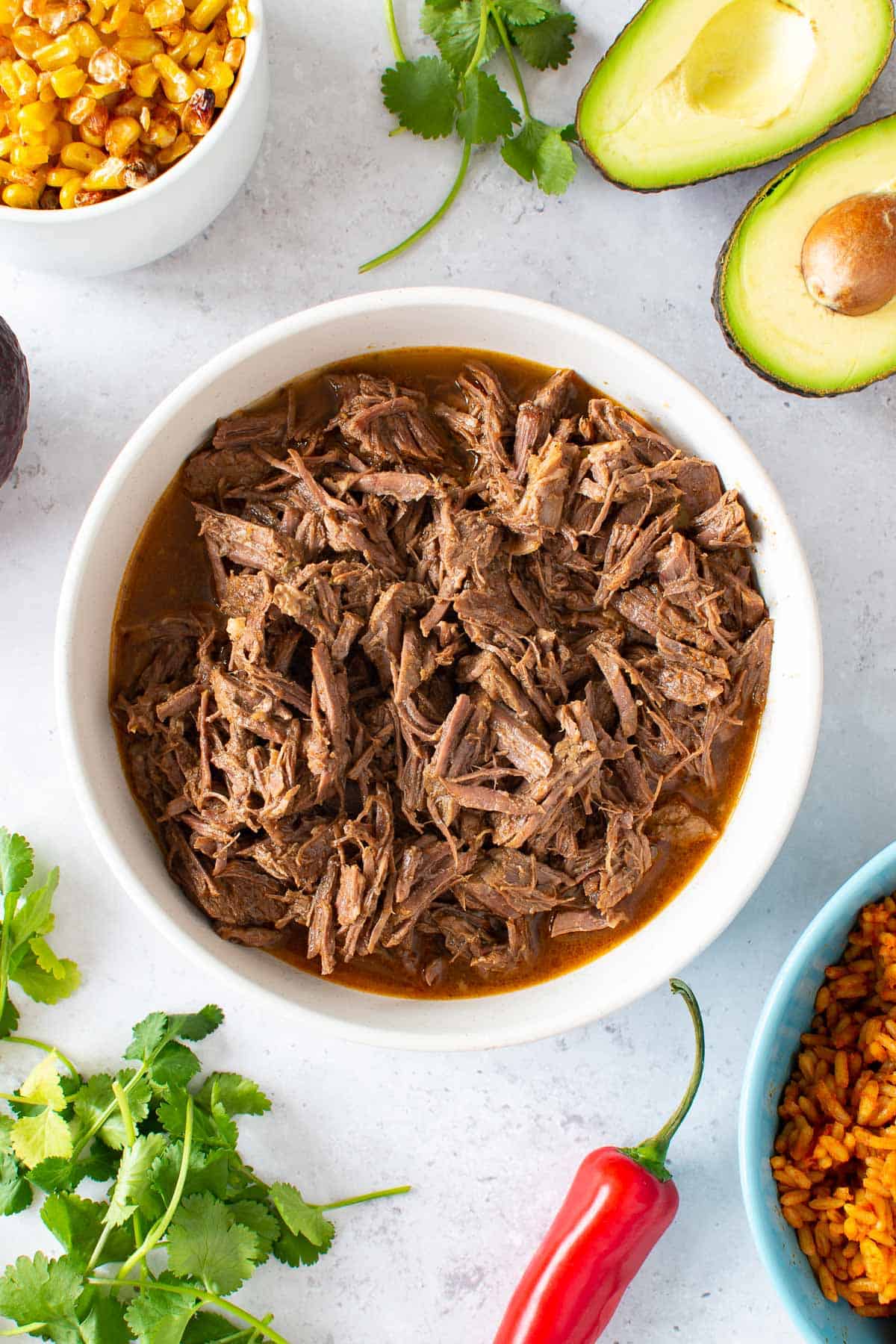 Instant Pot shredded beef with corn, avocado, cilantro and chili on the side.,