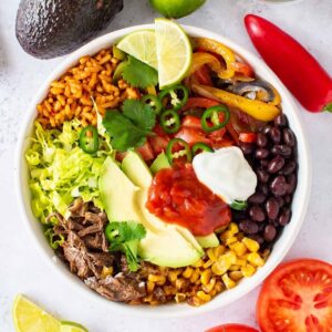 Bowl with Mexican rice, shredded beef, avocado, corn, peppers, black beans and salsa.