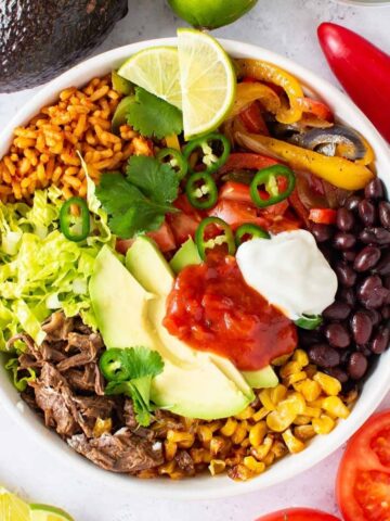 Bowl with Mexican rice, shredded beef, avocado, corn, peppers, black beans and salsa.