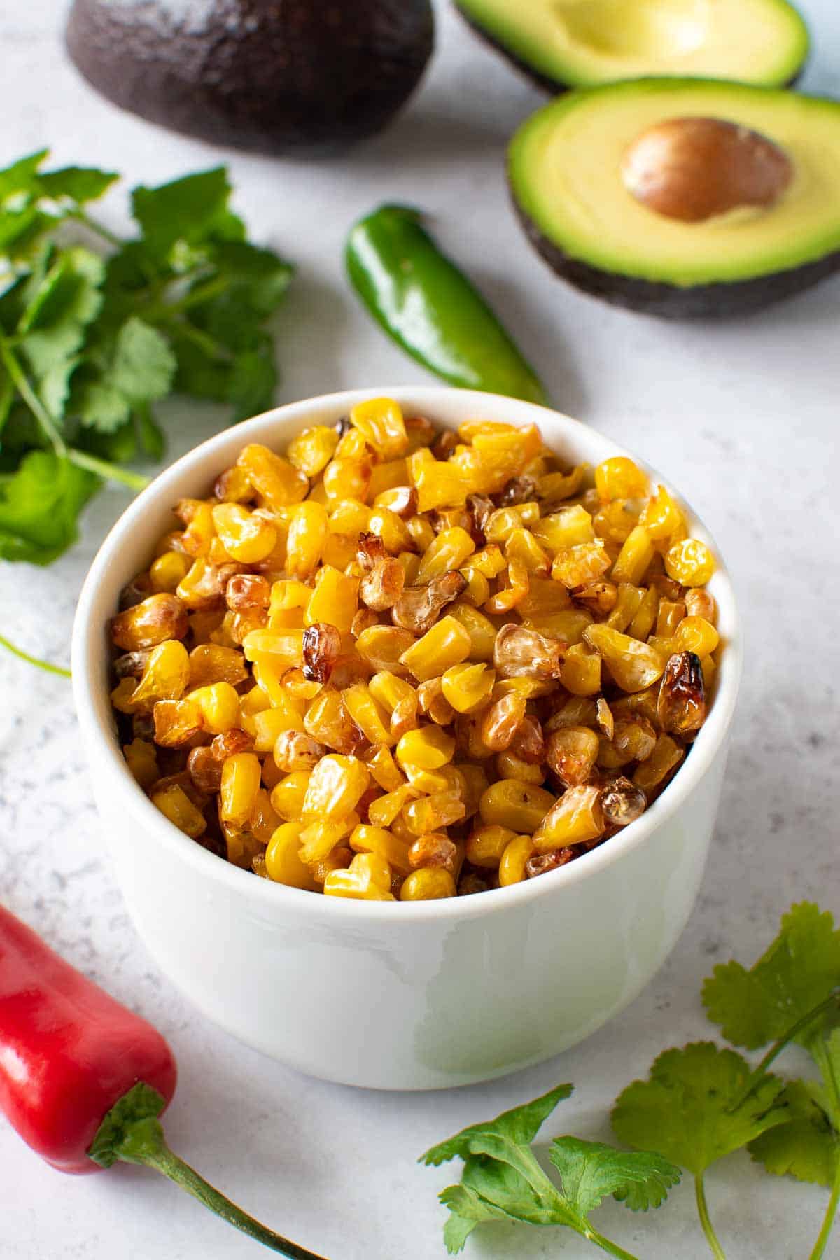 Roasted frozen corn in a bowl, with chilies and avocado in the background.