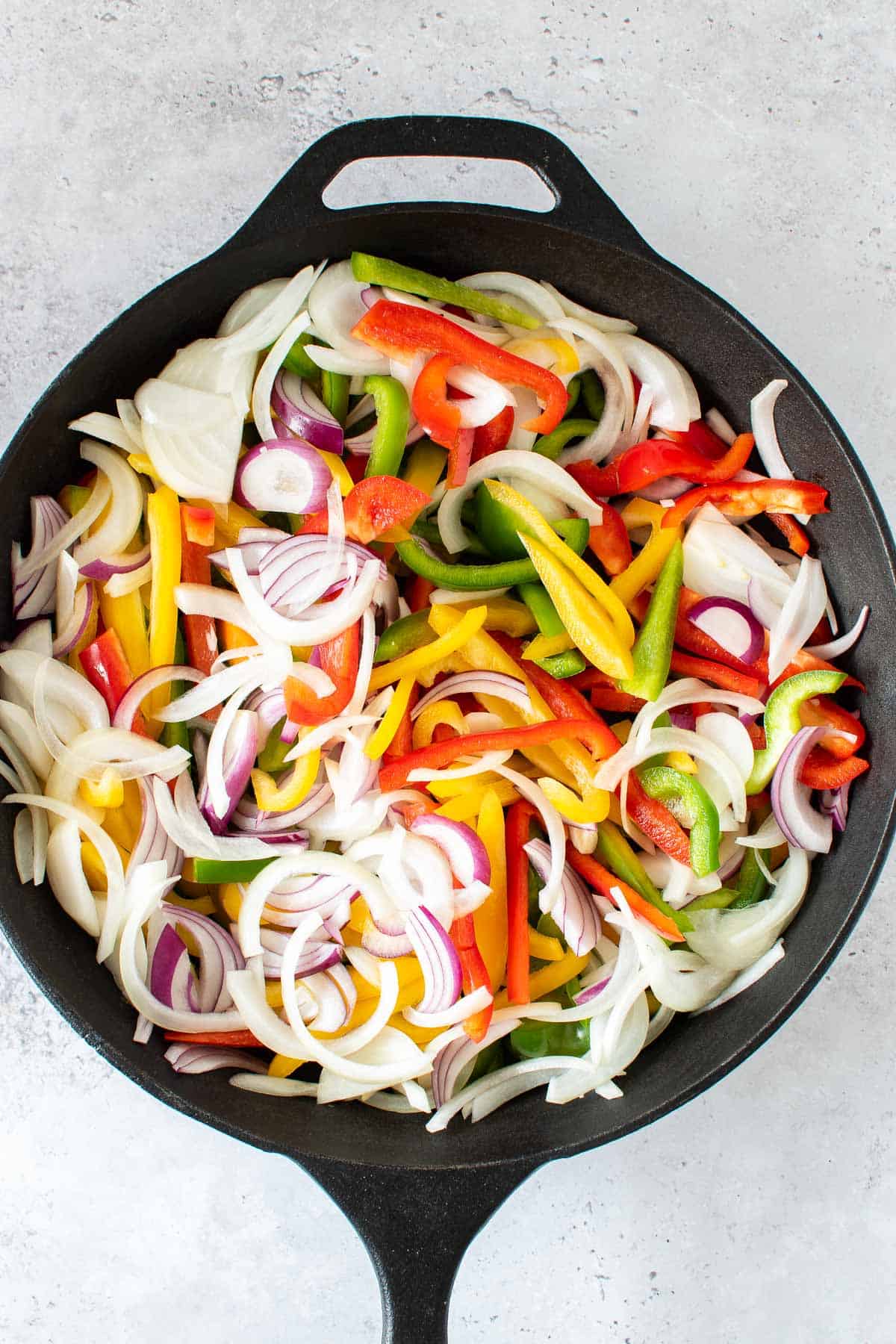 Raw sliced onions and peppers in a cast iron skillet.