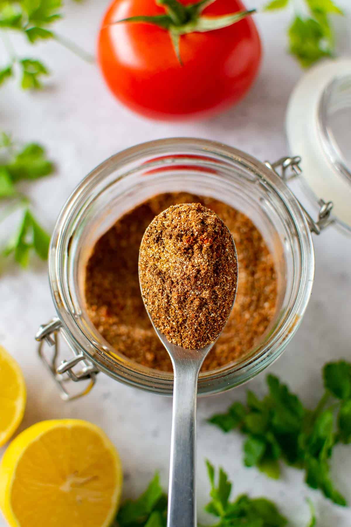 A spoon lifting up shawarma spice mix from a jar.