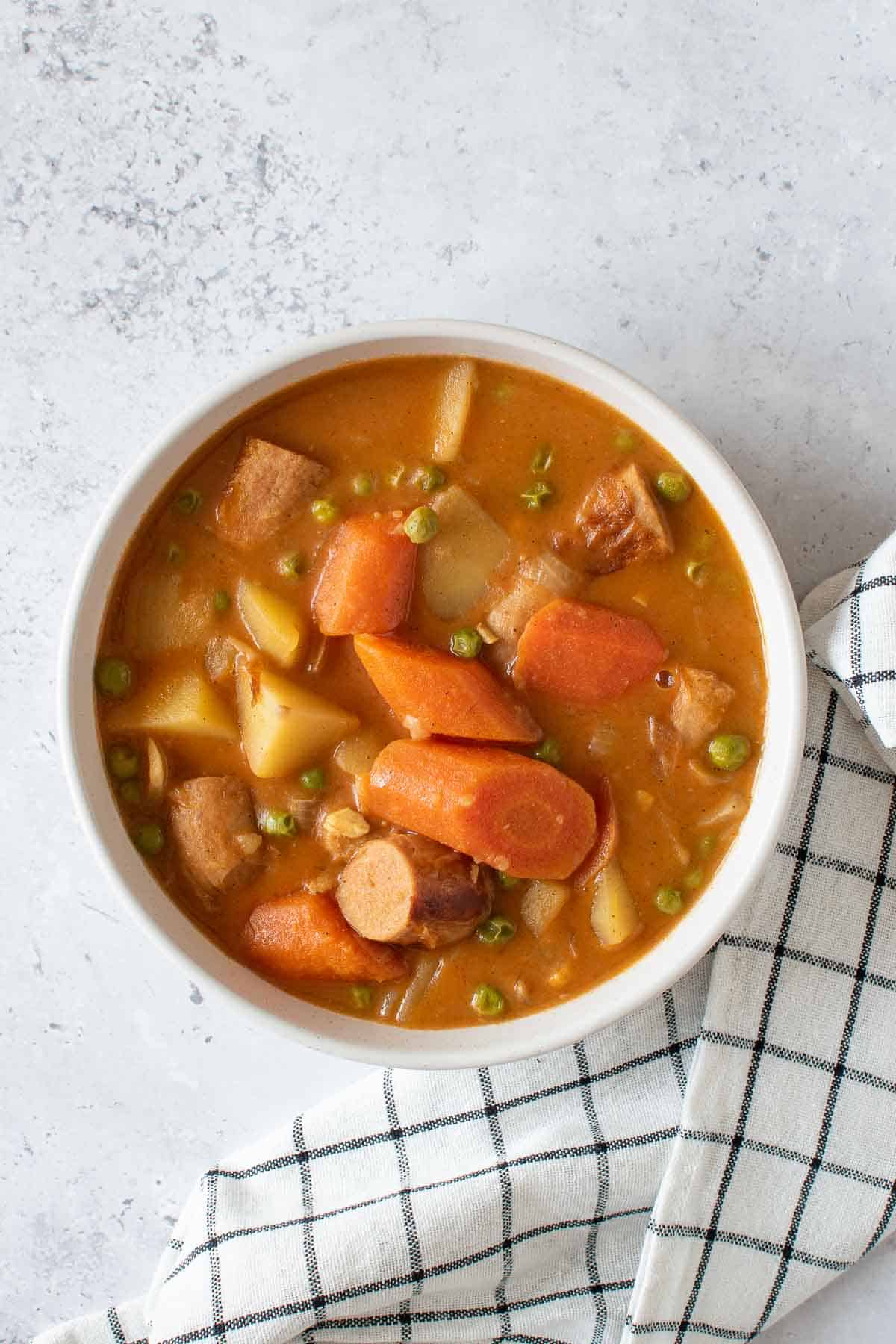 A bowl of curried sausages, potatoes, peas and carrots.