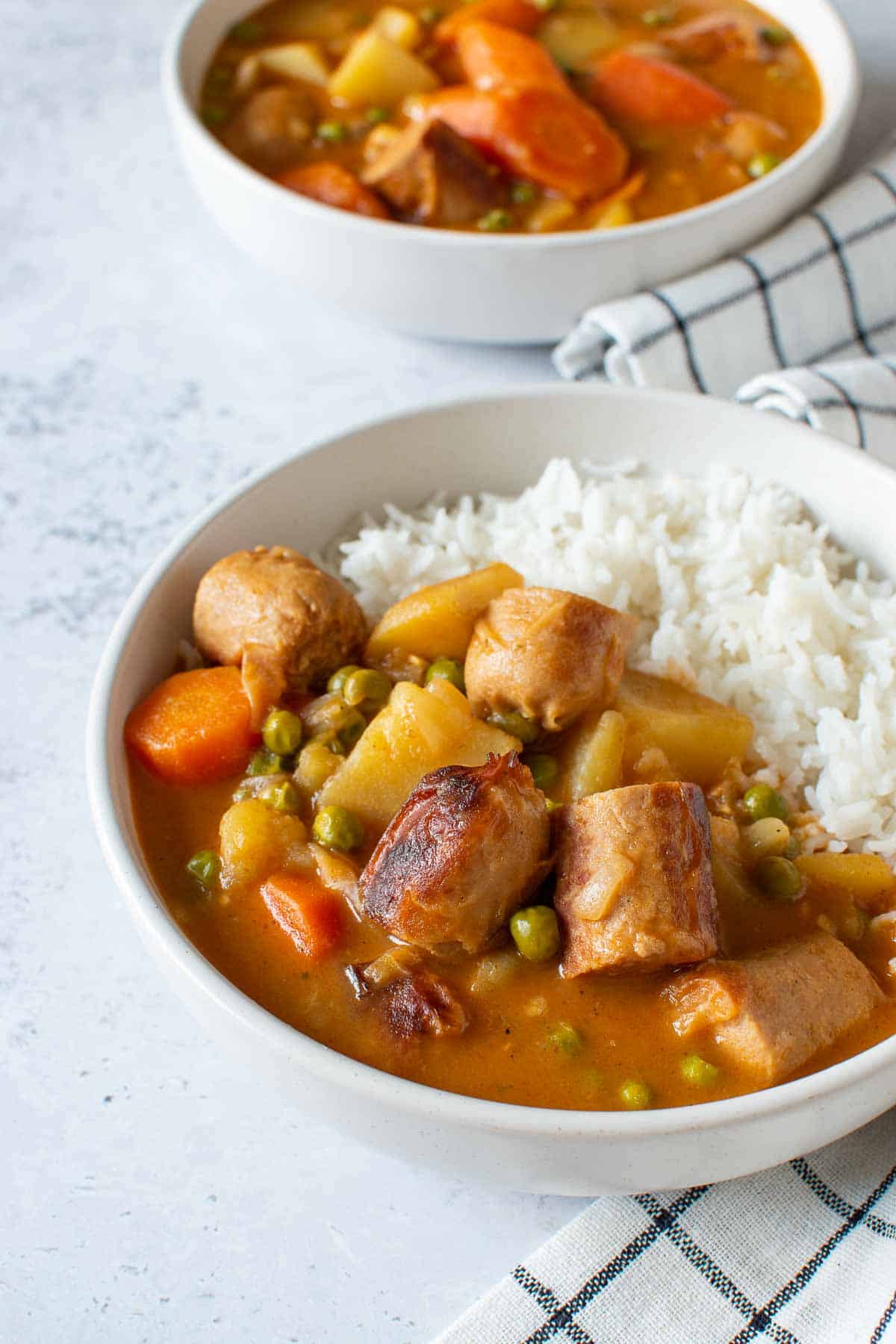 Curry with sausages, potatoes and carrots in a bowl with rice.