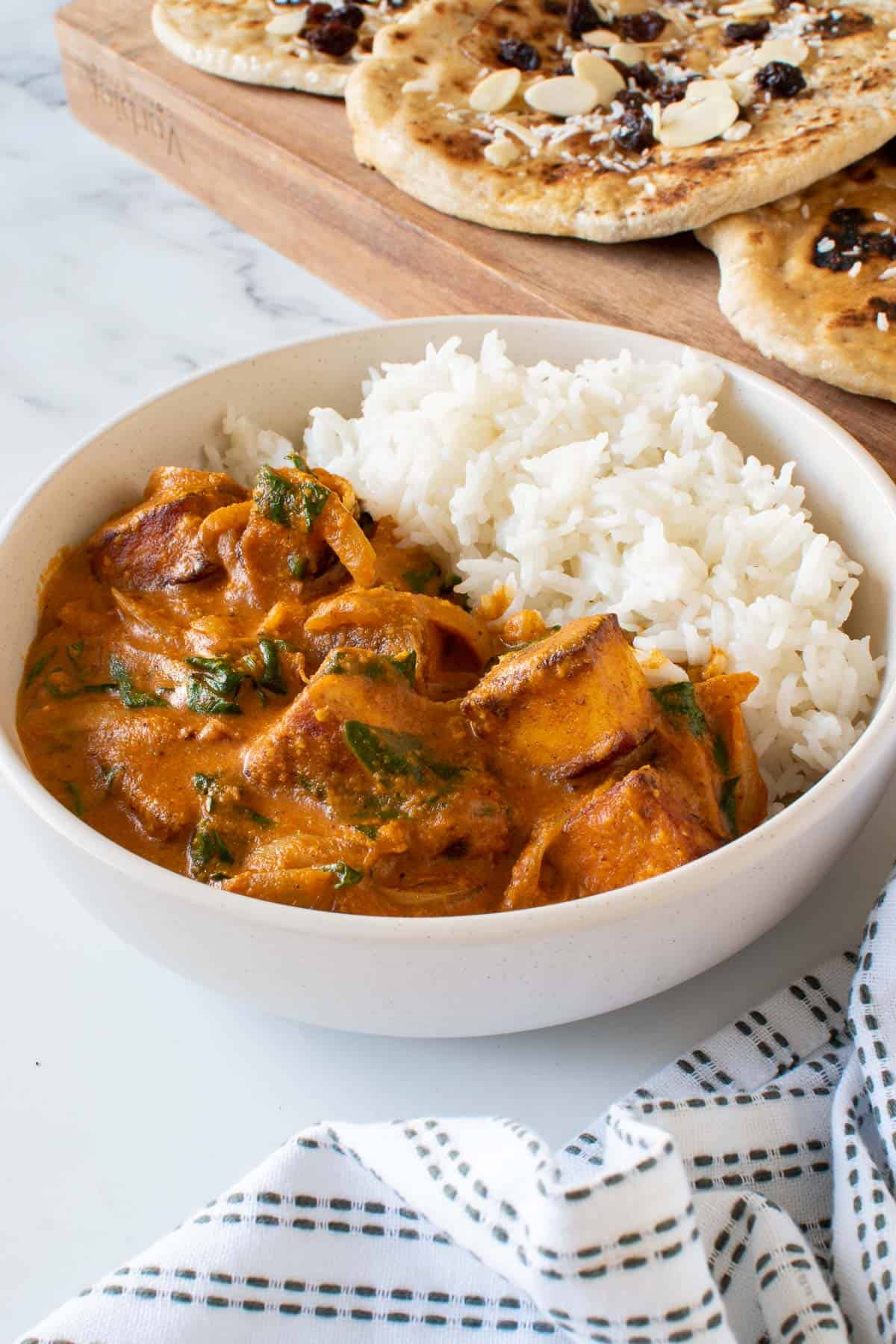 Onion and paneer korma curry served in a bowl with rice and naan.