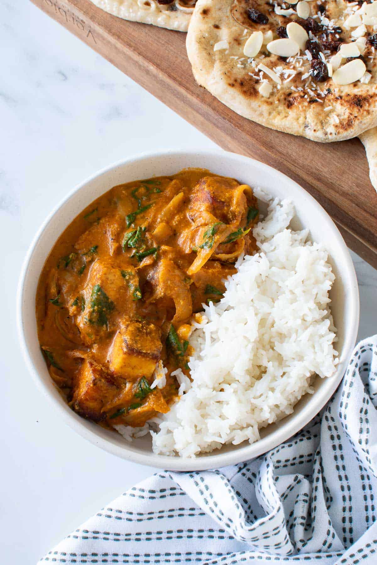 A bowl of paneer curry and rice, with naan on the side.