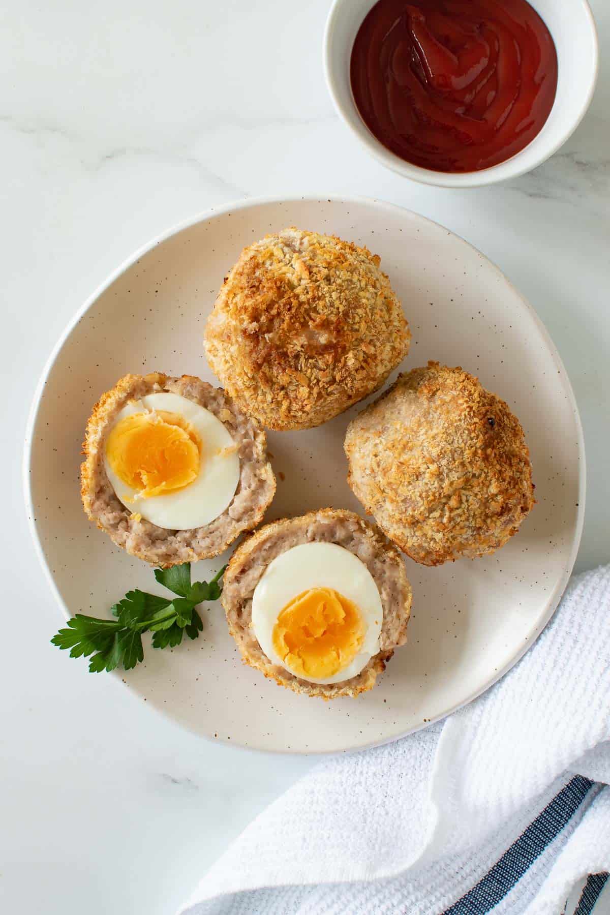 Air fried scotch eggs on a plate, with ketchup on the side.