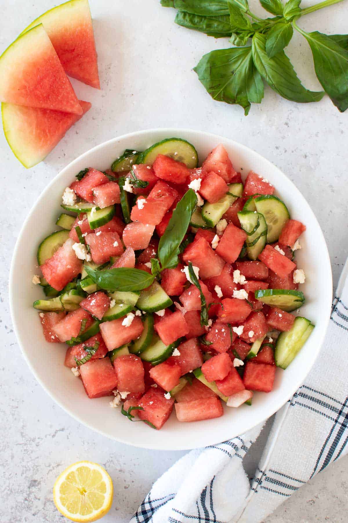 A bowl of watermelon basil salad, with watermelon, lemon and fresh basil on the side.