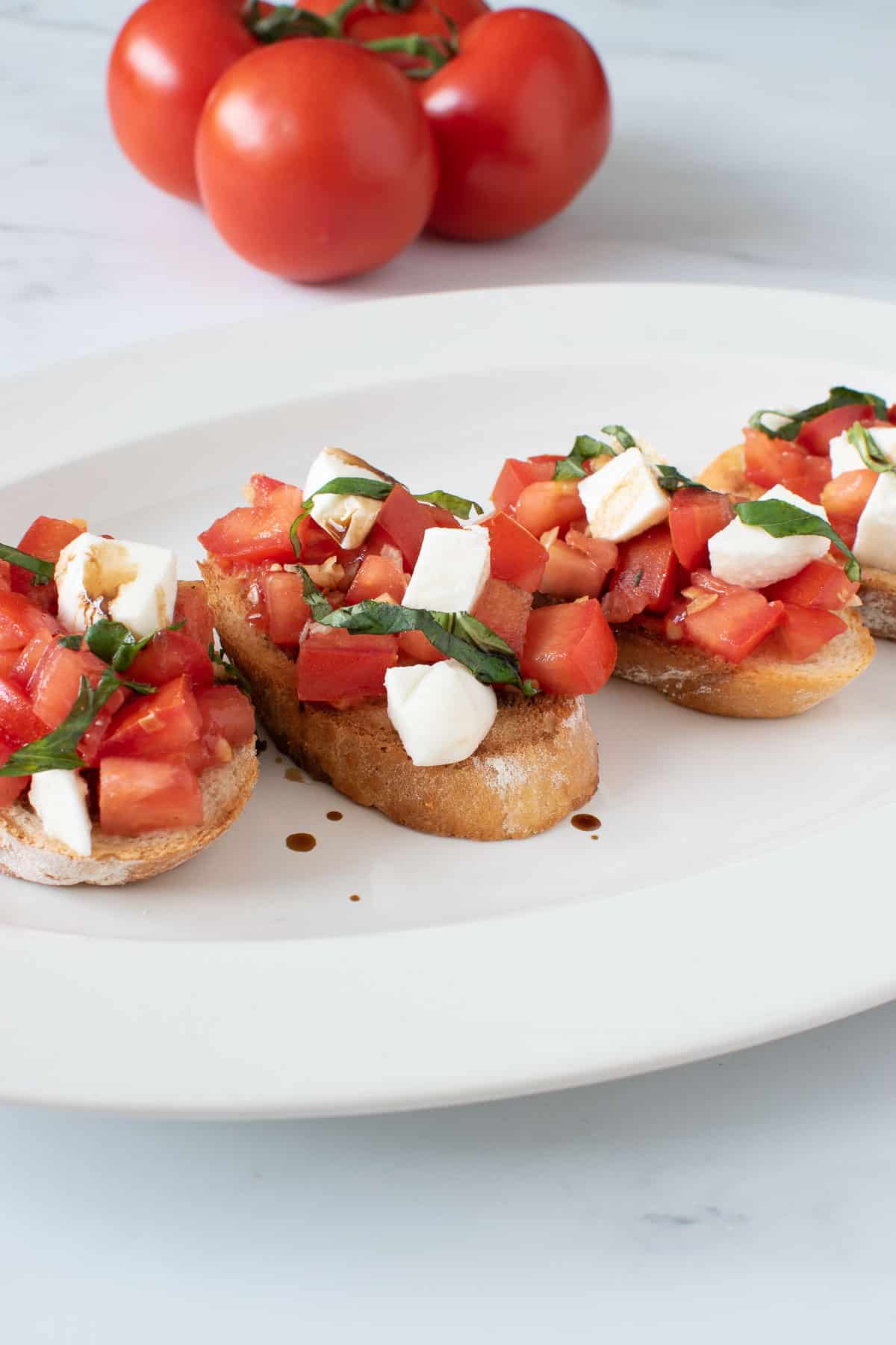 Caprese bruschetta on a plate, with tomatoes in the background.