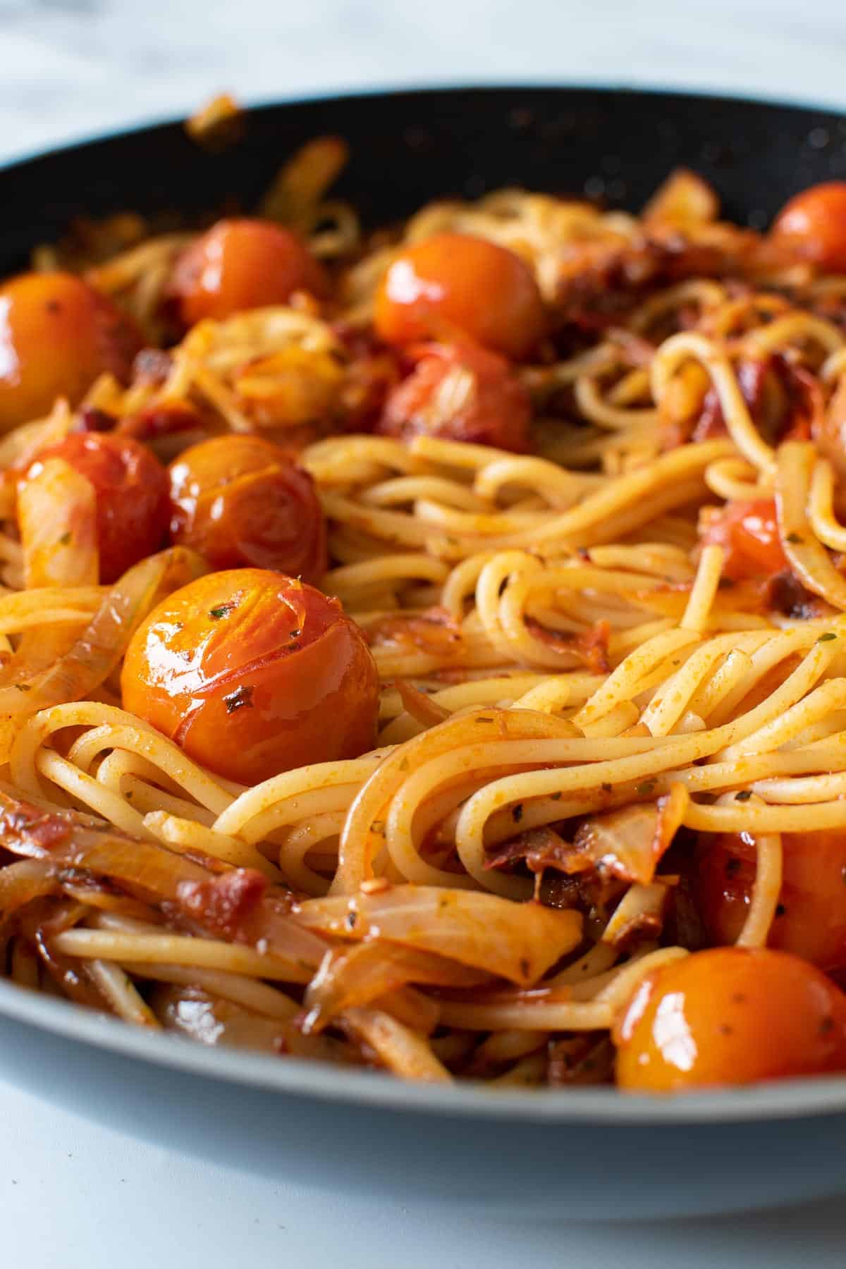 Close up of a pan with spaghetti with a spicy sauce and tomatoes.