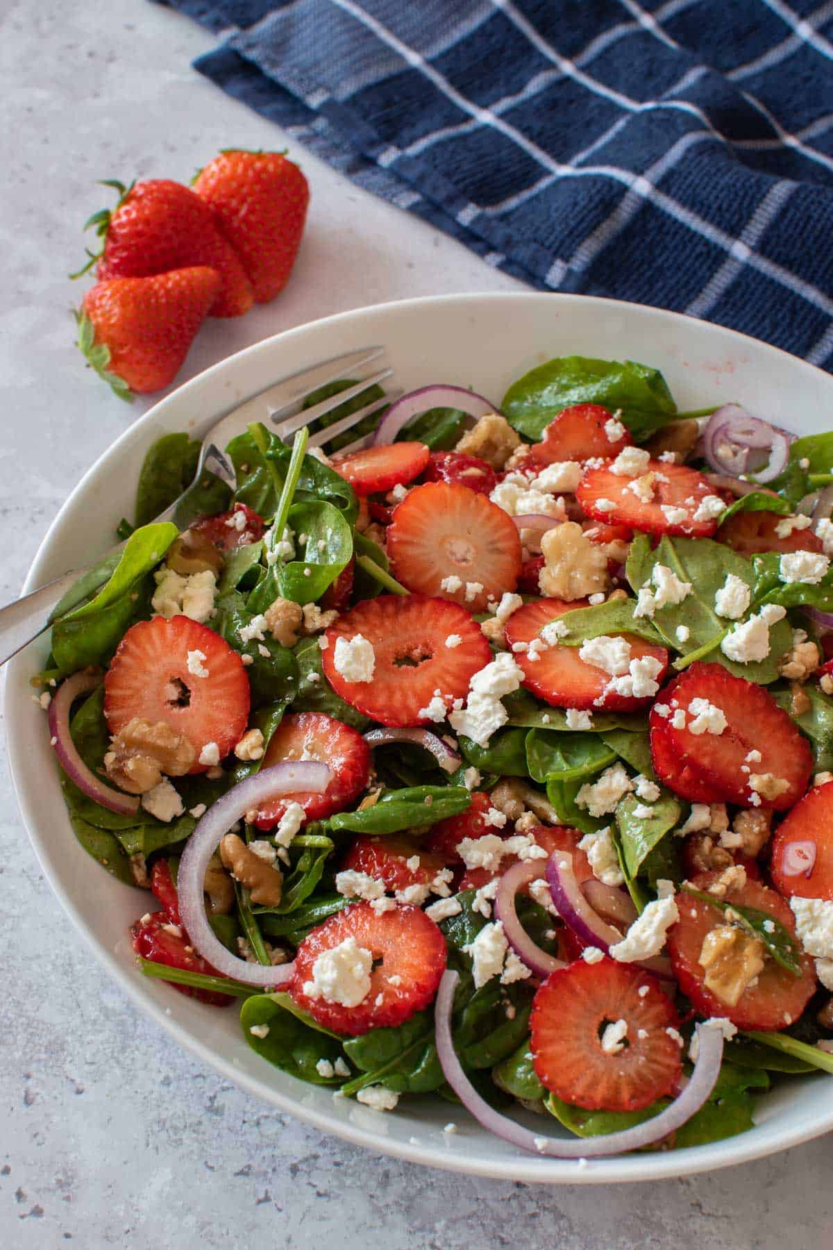 A bowl of walnut strawberry salad, with strawberries in the background.