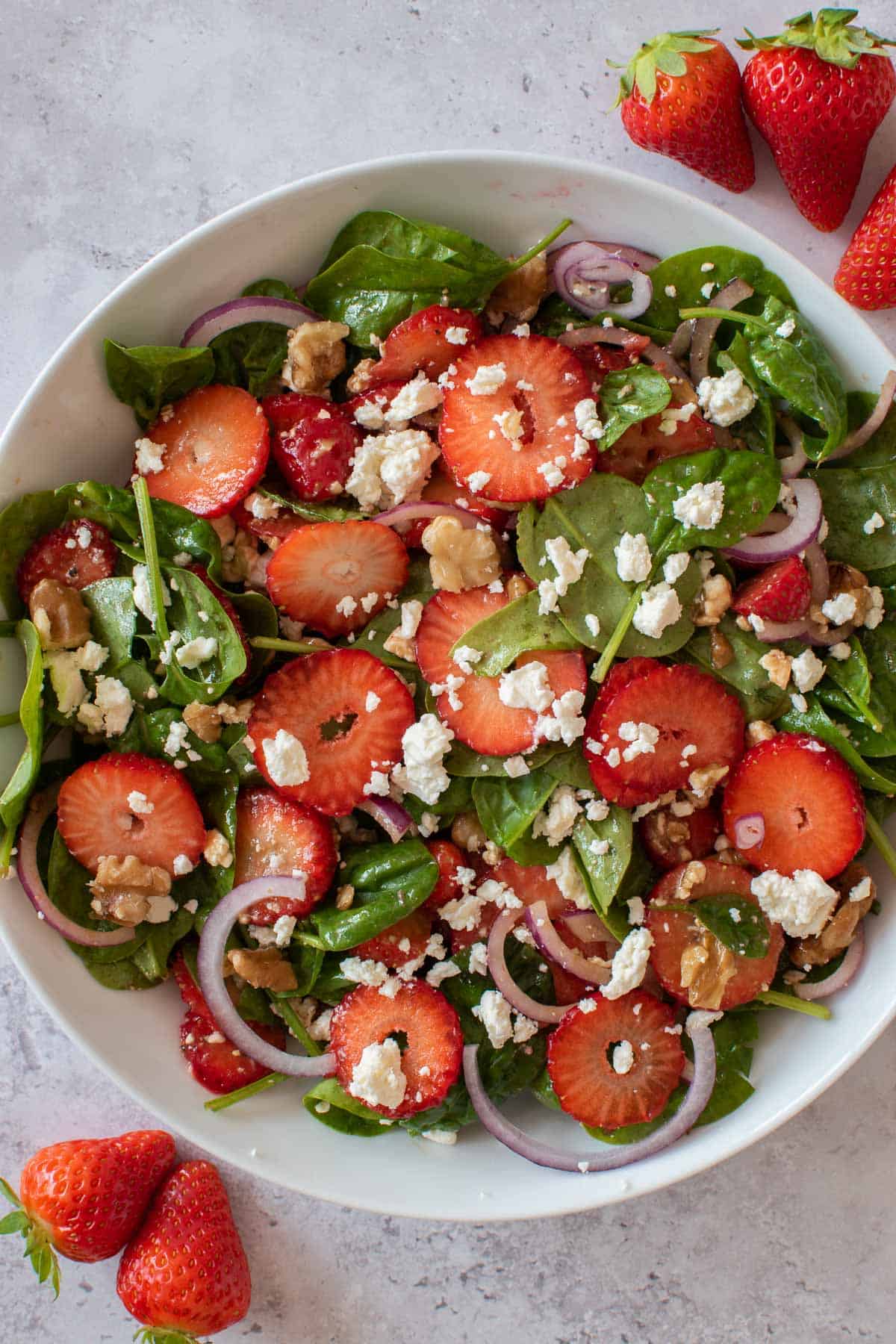A plate of mixed strawberry and walnut salad with feta cheese and spinach. Strawberries are scattered on the side.