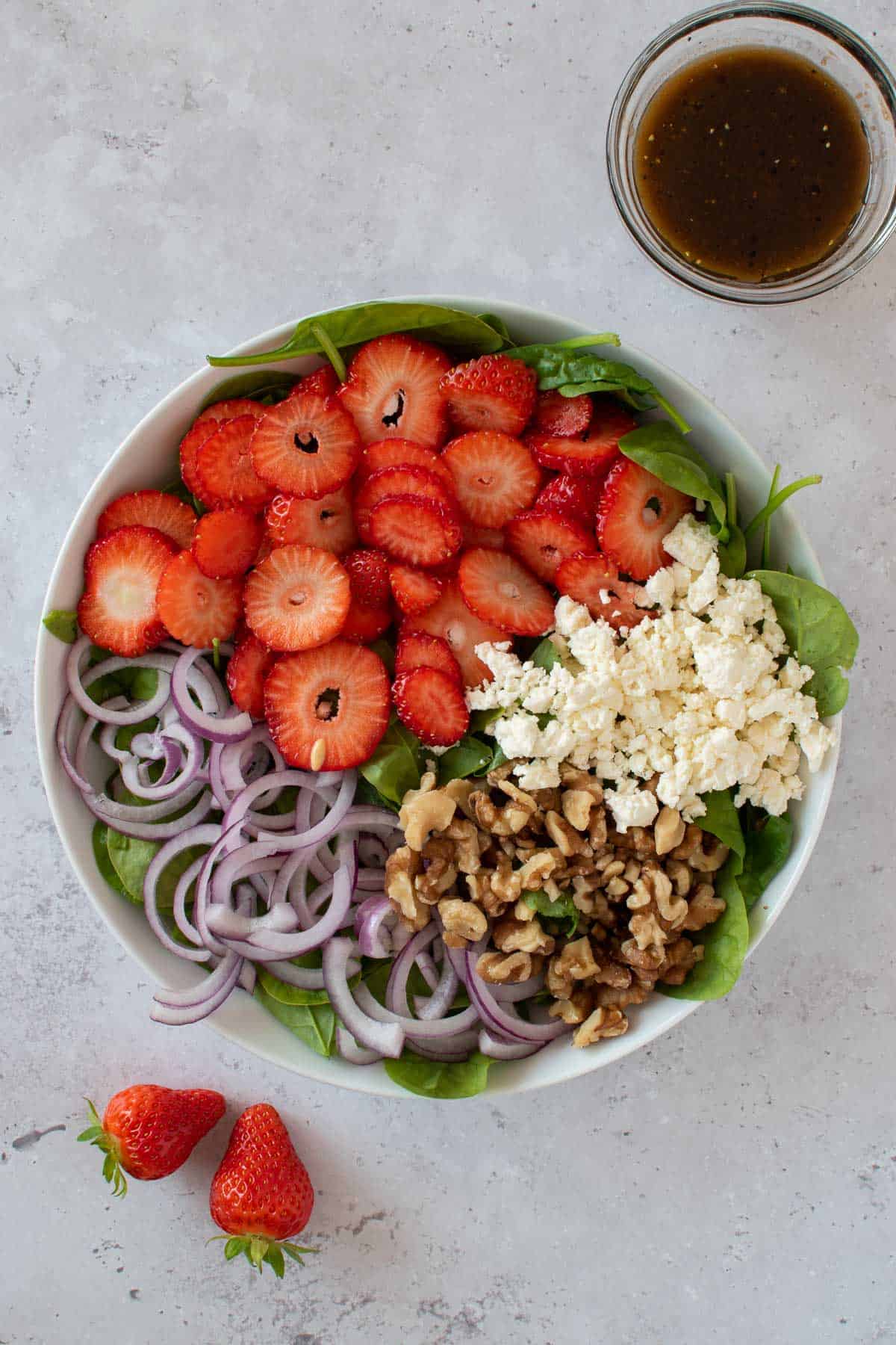 Spinach, strawberries, feta cheese, walnuts and red onions in a bowl.
