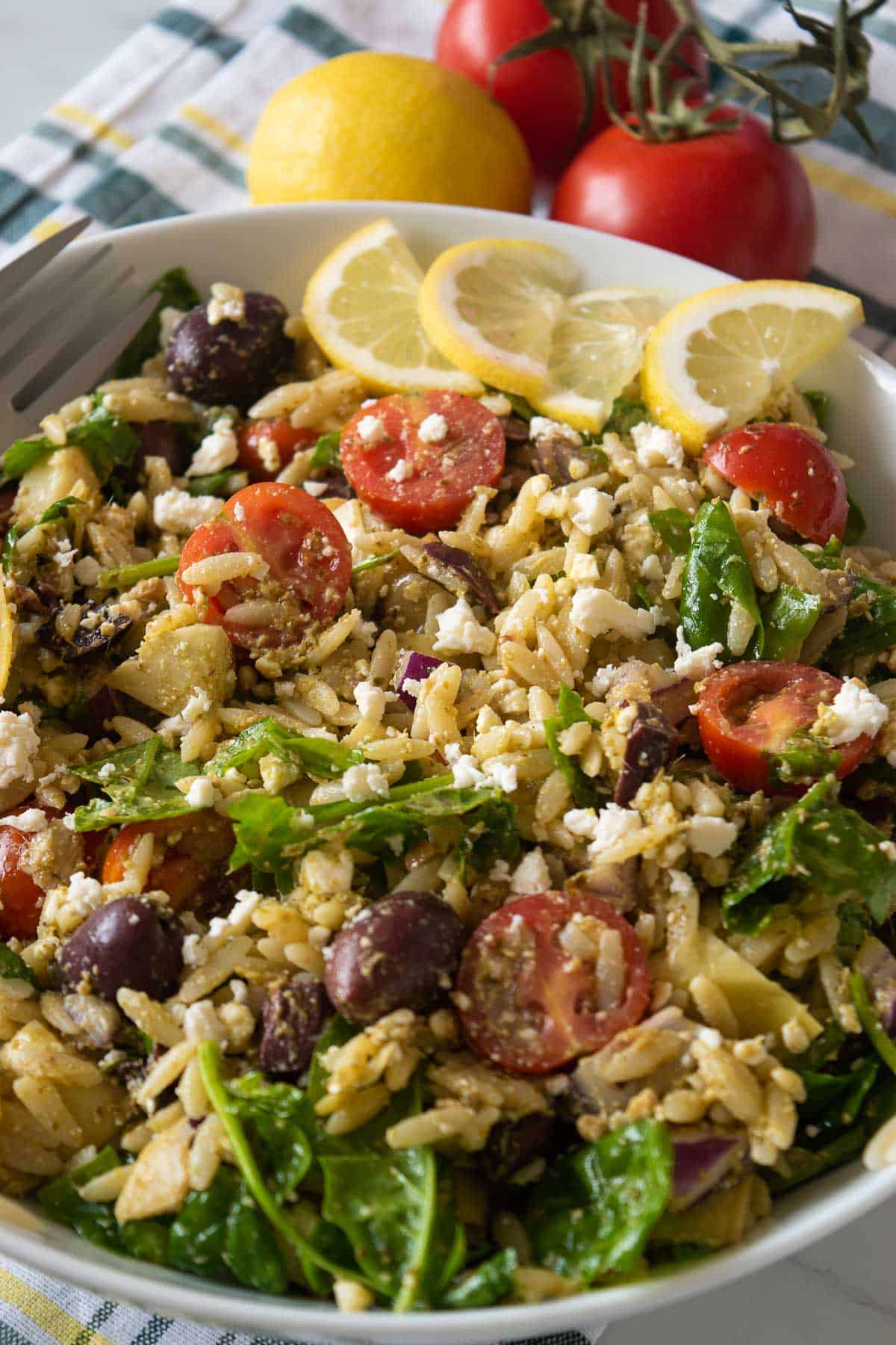 Close up of the orzo pesto salad with olives and tomatoes. Tomatoes and a lemon in the background.