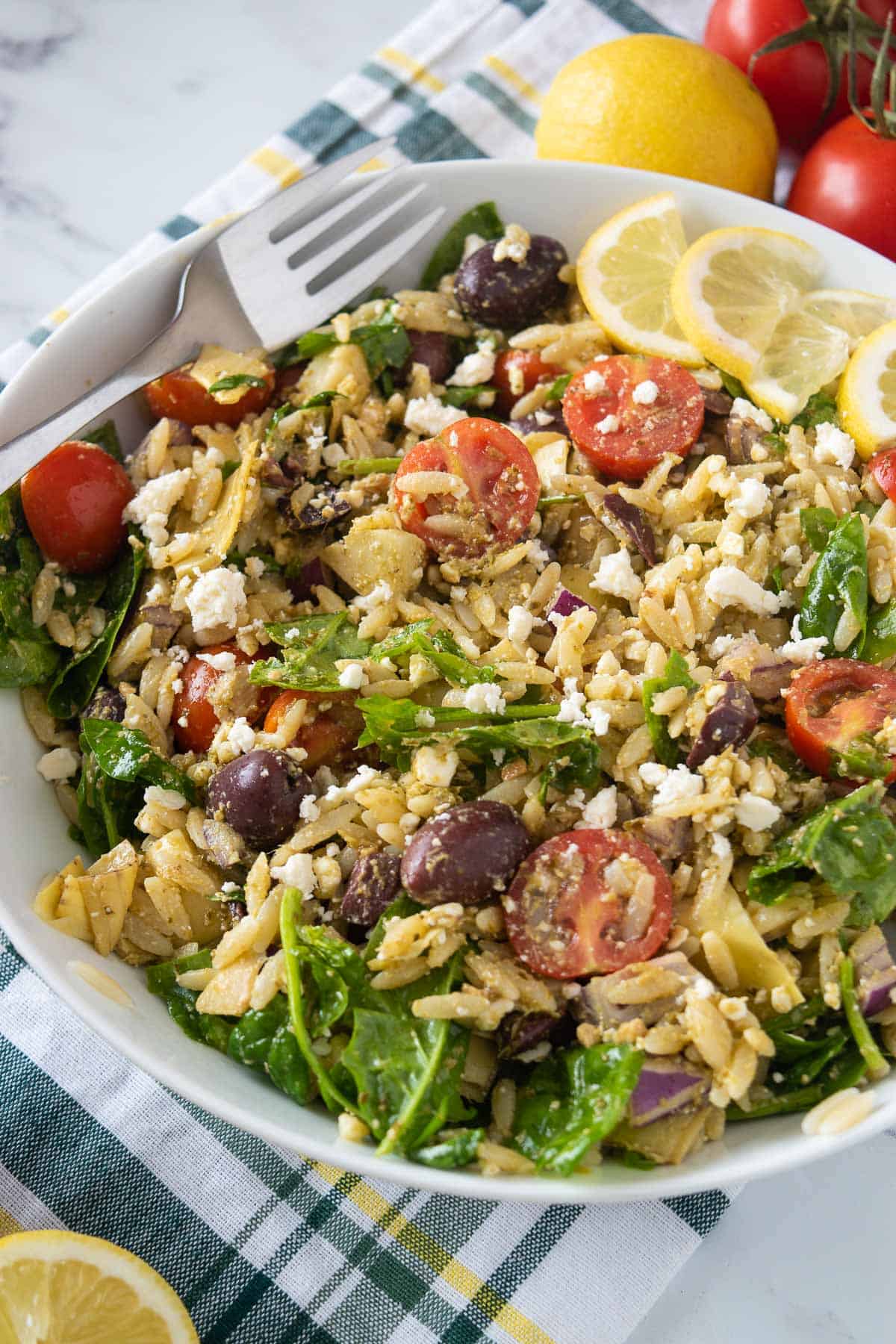 A bowl of orzo pesto salad with vegetables, and a fork on the side.