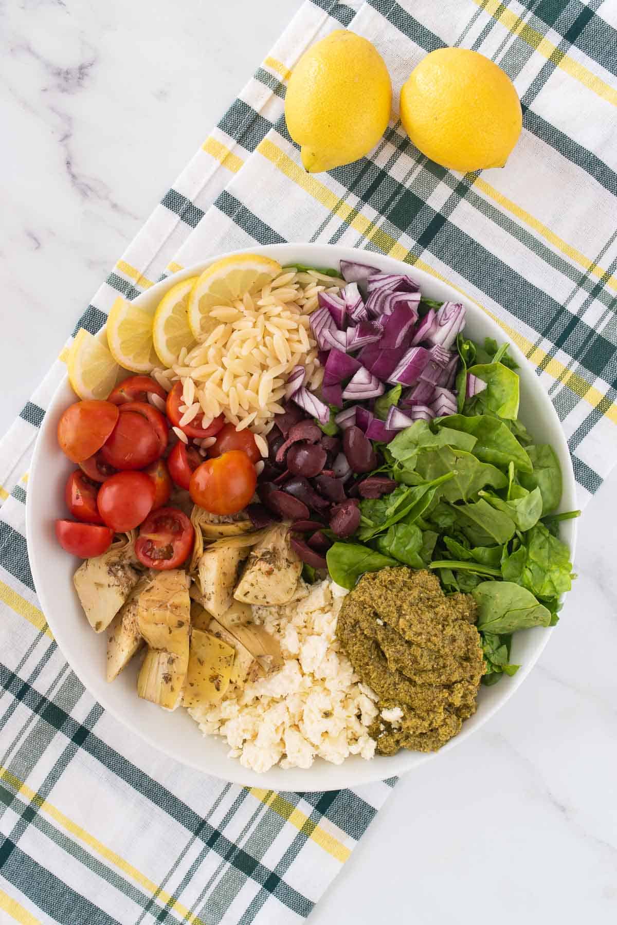 The ingredients for the orzo salad in a bowl, but they are not mixed yet.