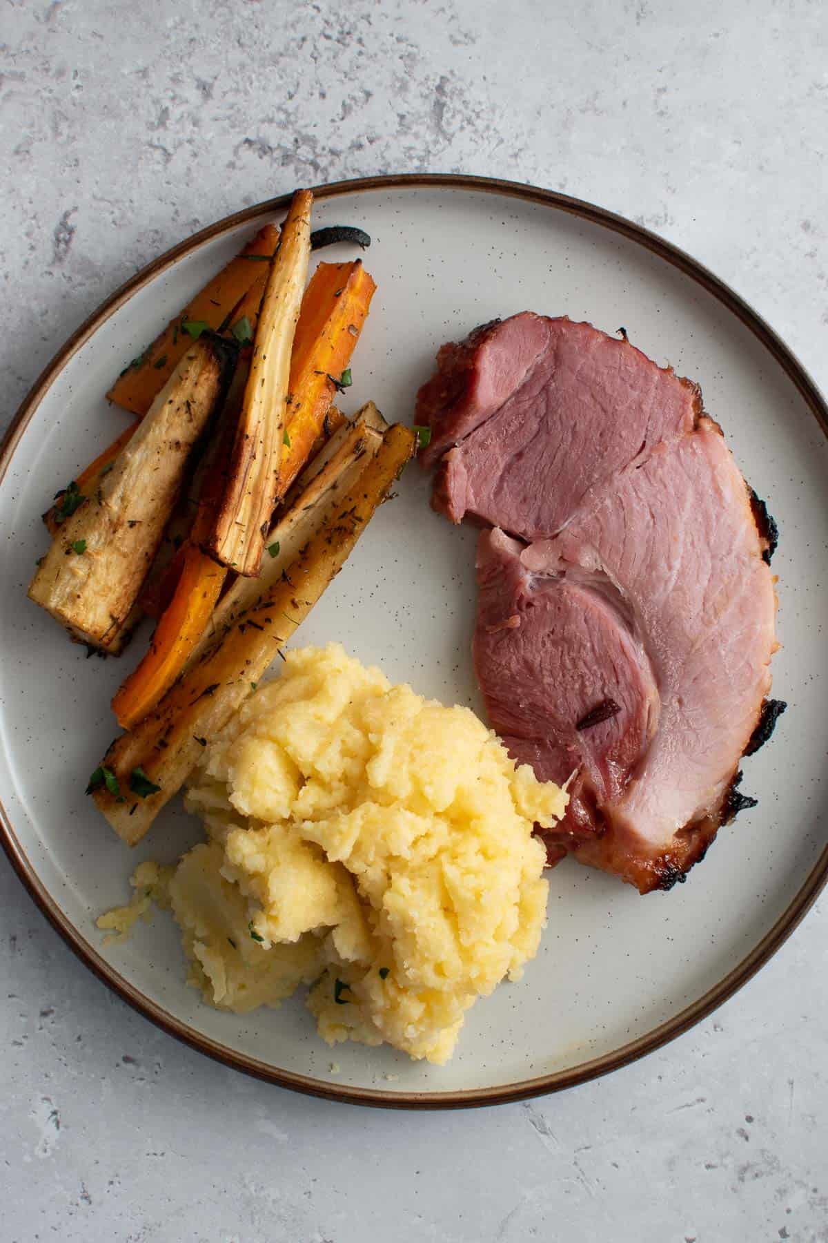 A plate with swede mash, honey roasted parsnips and carrots, and air fryer gammon.
