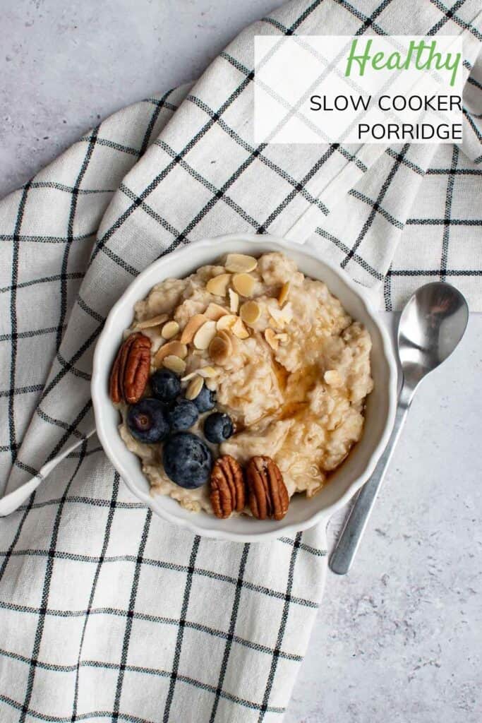 A bowl of slow cooker porridge, topped with nuts and blueberries. A tablecloth and spoon are on the side.