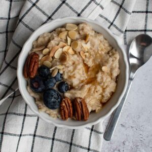 Slow cooked porridge in a bowl, topped with almonds, pecans, blueberries and maple syrup.