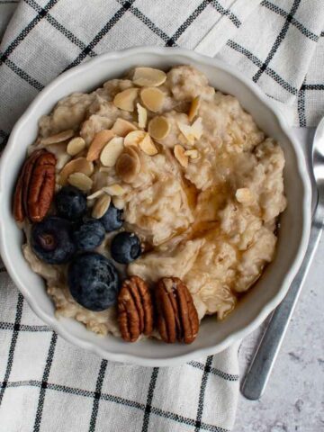 Slow cooked porridge in a bowl, topped with almonds, pecans, blueberries and maple syrup.