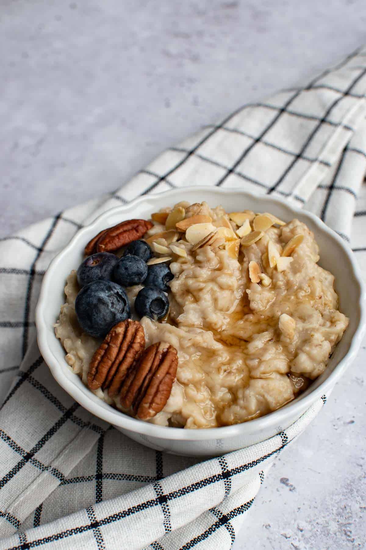 A bowl of slow cooker oatmeal, garnished with almonds, blueberries, pecans and maple syrup.